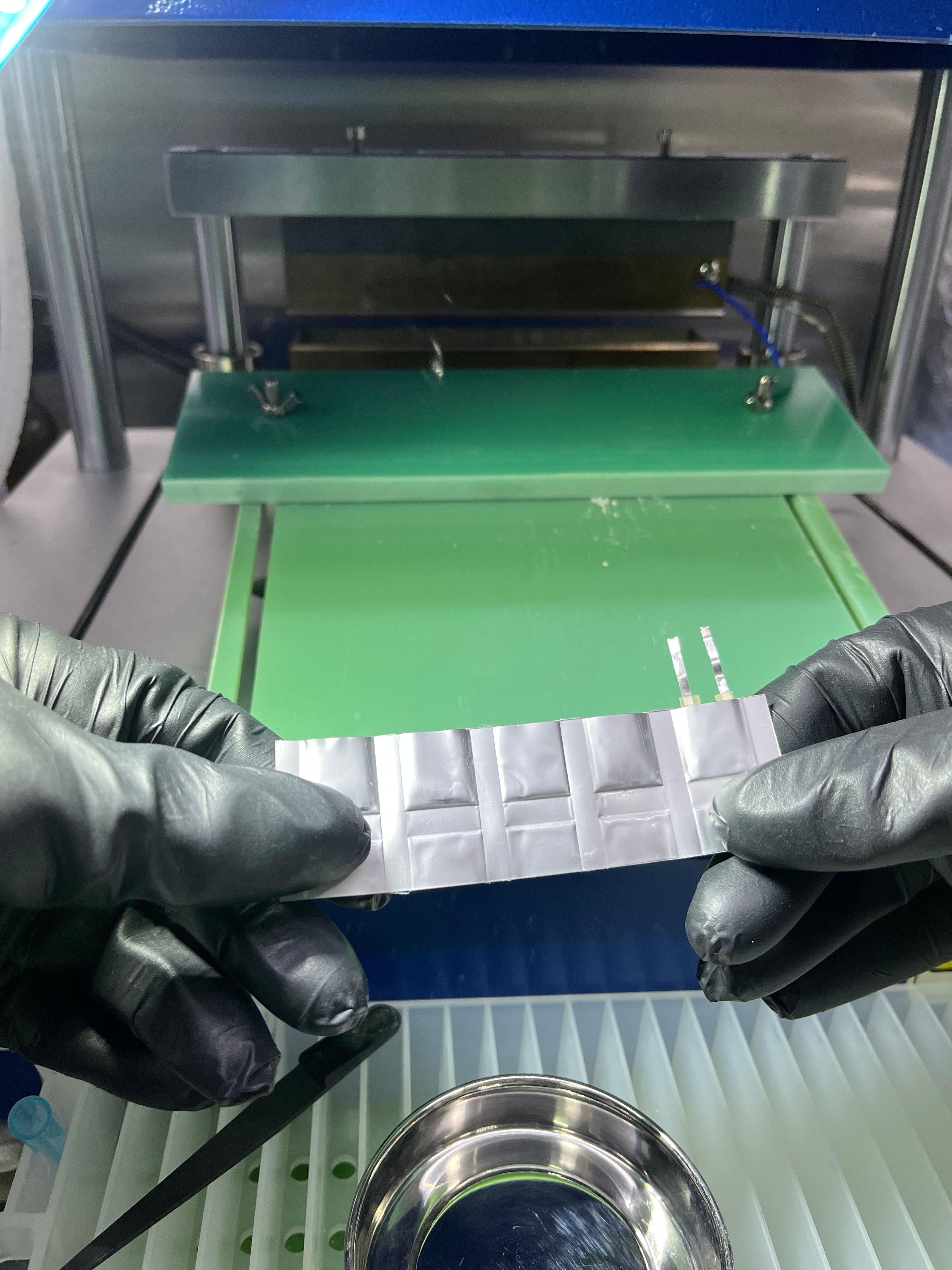 Gloved hands holding a set of Volfpack pouch-cell prototypes